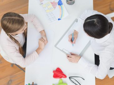 an-elevated-view-of-little-girl-talking-with-her-female-psychologist-taking-note-on-clipboard-scaled-e1648667934511.jpg